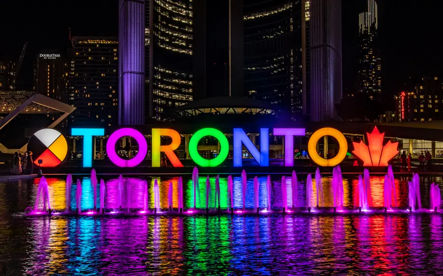 Illuminated Toronto sign and fountain at Nathan Phillips Square at night.